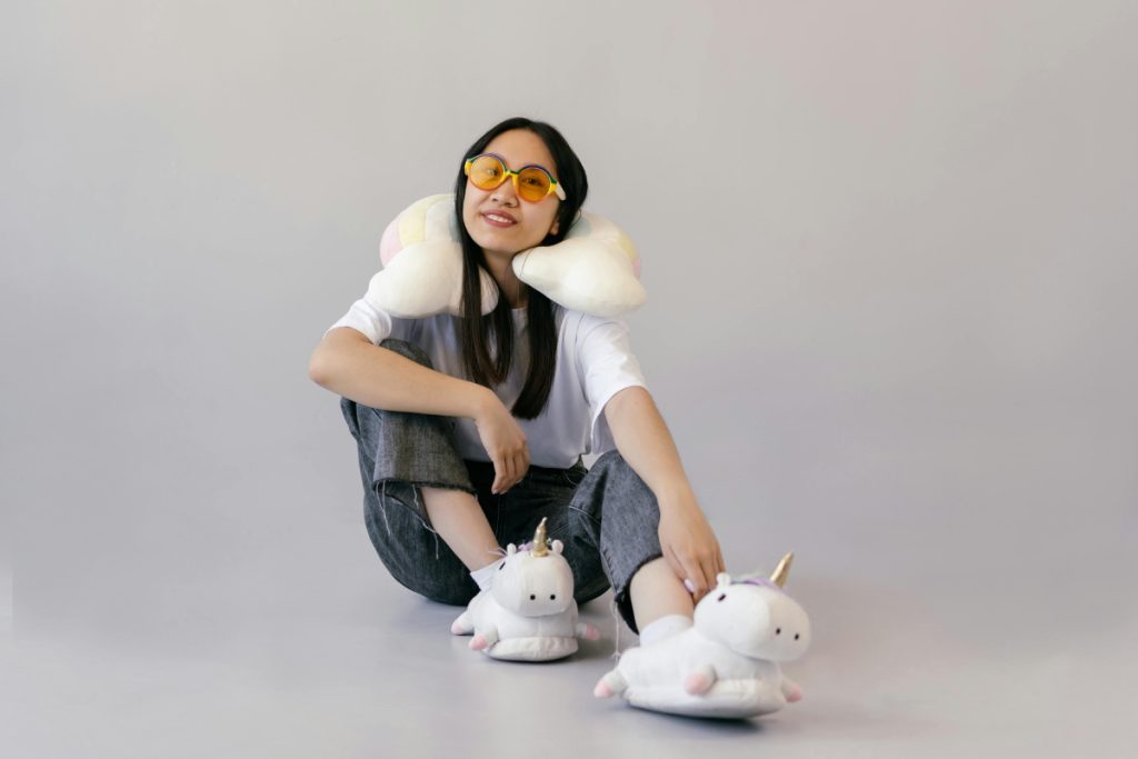 woman sitting on floor wearing a grey travel pillow around her neck